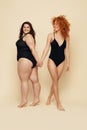 Different Size. Diversity Women Full-Length Portrait. Smiling Brunette And Redhead In Black Bodysuits Posing On Beige Background. Royalty Free Stock Photo