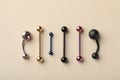 Different stylish barbells on beige background, flat lay. Piercing jewelry