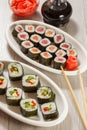 Different sushi rolls on ceramic plates, chopsticks, glass bottle with soy sauce and pickled ginger in a bowl Royalty Free Stock Photo