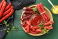 Different thin dry smoked sausages, parsley and sauces on green wooden table, flat lay Royalty Free Stock Photo