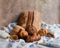 Different types of baking still life. Buns croissants, muffins and loaves, bread patties on textile drapery with flower