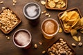 Craft drinks in glasses and pistachios, nuts, crackers, crisps and chips in plate and scattered on wooden table Royalty Free Stock Photo