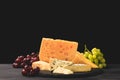 Different types of cheese on board with grapes on black