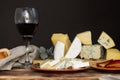 Different types of cheese on a wooden cutting board on a dark background with an apple and a glass of wine. Copy space Royalty Free Stock Photo