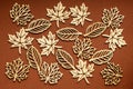 Different types of delicate light brown wooden leaves on textured brown cardboard, top view or flat lay with laser cut wooden obje