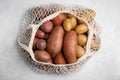 Different types of fresh potatoes in net bag on light gray table, top view Royalty Free Stock Photo