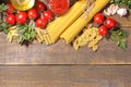 Different types of pasta with cherry tomatoes, olive oil, parsley on a brown wooden background.