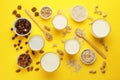 Different vegan milks and ingredients on yellow background, flat lay