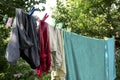 Different washed clothes is dried on rope in backyard or garden. Drying linen with multicolored clothespins. Summer sunny day. Royalty Free Stock Photo