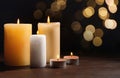 Different wax candles burning on table against dark background with blurred lights. Bokeh effect Royalty Free Stock Photo