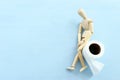 digestion or constipation health problen. Wooden figure sit on a roll of toilet paper. blue background