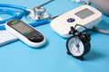 blood pressure monitor, glucometer, stethoscope, notepad and alarm clock on blue background