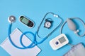 Digital blood pressure monitor, glucometer, stethoscope, notepad and alarm clock on blue background top view