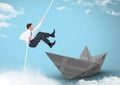 Businesman swinging on rope with paper boat in sky Royalty Free Stock Photo