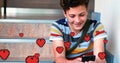 Digital composite of a Caucasian boy sitting in the stairs smiling while texting and digital hearts Royalty Free Stock Photo