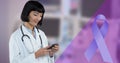 Digital composite image of blue ribbon and smiling asian young female doctor using smart phone Royalty Free Stock Photo