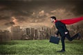 Digital composite image of businesswoman wearing cape running on field against city Royalty Free Stock Photo