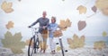 Digital composite image of multiple leaves against senior couple walking with bicycle at the beach