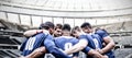 Digital composite image of team of rugby players standing in a huddle in sports stadium Royalty Free Stock Photo