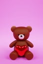 Digital 3D render of a cute romantic brown teddy bear figure with a heart on a pink background