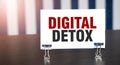 DIGITAL DETOX sign on paper on dark desk in sunlight. Blue and white background