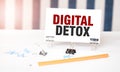 DIGITAL DETOX sign on paper on white desk with office tools. Blue and white background