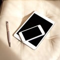 Digital devices - white smartphone and tablet on leather armchair.