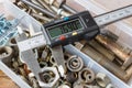 Digital electronic caliper on a background of opened storage box with rusty used bolts and nuts