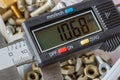 Digital electronic caliper on a background of opened storage box with used bolts and nuts closeup