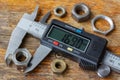 Digital electronic caliper with used nuts on wooden table in workshop