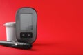 Digital glucometer, lancet pen and container on red background, space for text. Diabetes control