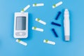 Digital glucometer, lancet pen, disposable needles and test strips on pastel blue background. Top view. Diabetes concept