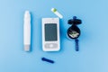 Digital glucometer, lancet pen, disposable needles and test strips on pastel blue background. Top view. Diabetes concept