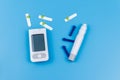 Digital glucometer, lancet pen, disposable needles and test strips on pastel blue background. Top view. Diabetes concept