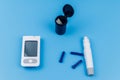 Digital glucometer, lancet pen, disposable needles and test strips on pastel blue background. Top view. Diabetes concept