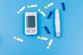 Digital glucometer, lancet pen, disposable needles and test strips on pastel blue background. Top view. Diabetes concept