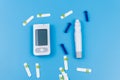 Digital glucometer, lancet pen, disposable needles and test strips on pastel blue background. Top view. Diabetes concept