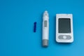 The digital glucometer and lancet pen are isolated on blue background