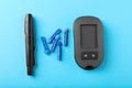 Digital glucometer, lancets and pen on light blue background, flat lay. Diabetes control