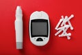 Digital glucometer, lancets and pen on red background, flat lay. Diabetes control