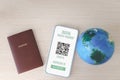 Digital health passport on mobile phone showing vaccination certification with passport and earth globe on wooden board, safety