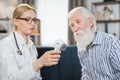 Digital infrared thermometer in hand of pleasant blond 40-aged woman doctor or nurse, visiting her senior male patient Royalty Free Stock Photo