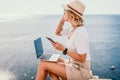 Digital nomad, Business woman working on laptop by the sea. Pretty lady typing on computer by the sea at sunset, makes a