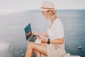 Digital nomad, Business woman working on laptop by the sea. Pretty lady typing on computer by the sea at sunset, makes a