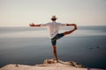 A digital nomad, a man in a hat, a businessman does yoga on the rocks by the sea at sunset time, does a business