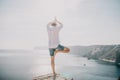 A digital nomad, a man in a hat, a businessman does yoga on the rocks by the sea at sunset time, does a business