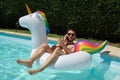 Digital nomad wearing sunglasses talking on the phone backwards on a unicorn inflatable ring in a swimming pool