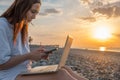 Digital nomad woman working with laptop and mobile phone on the beach by the sea during sunset. Female freelancer work Royalty Free Stock Photo