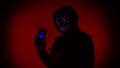 Digital security Concept. Anonymous hacker with mask holding smartphone hacked