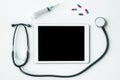 Digital tablet with blank on a medical desk with stethoscope, syringe and pills